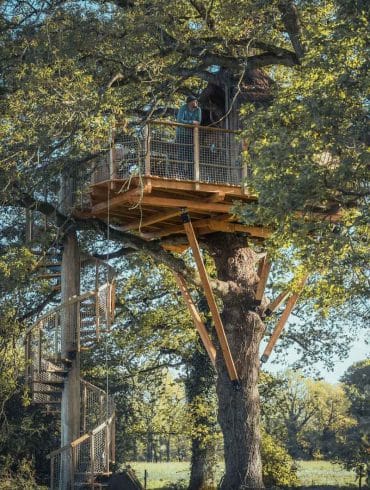 Homme admirant la vue panoramique sur la forêt depuis le balcon en bois d'une cabane perchée.