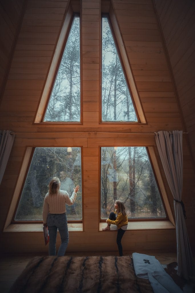 Mère et fille assises dans une cabane avec un toit cathédrale vitré offrant une vue sur les arbres