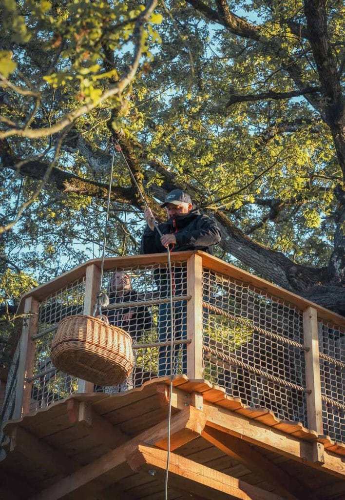 Père et fille hissant un panier-repas avec une corde jusqu'au balcon de leur cabane perchée